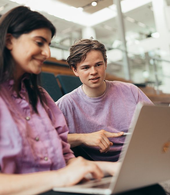 To studerende i lyserøde trøjer kigger på en computer